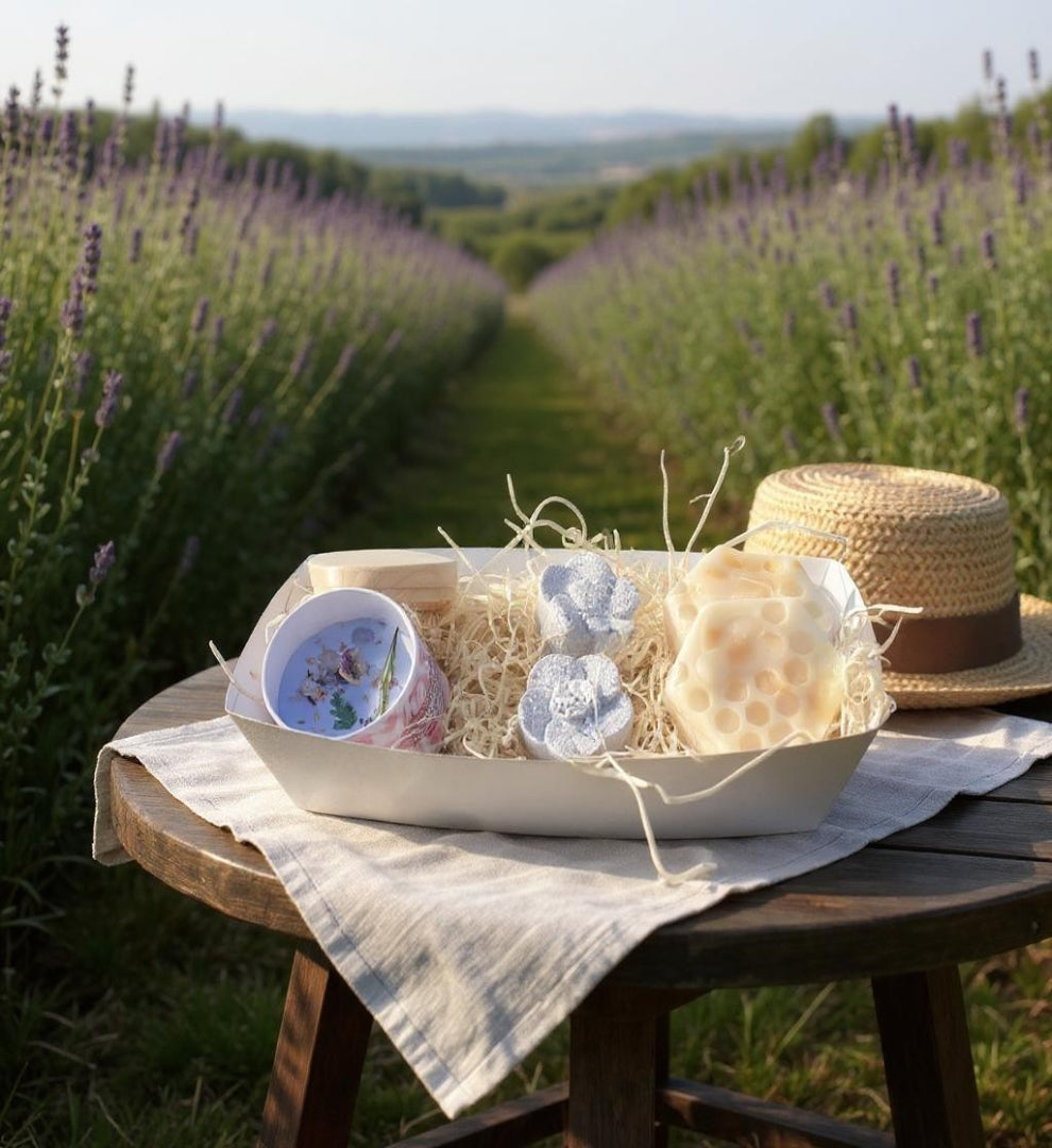 Table with a bowl of flowers and a hat in a lavender field and a lavender candle and soap, bath bombs