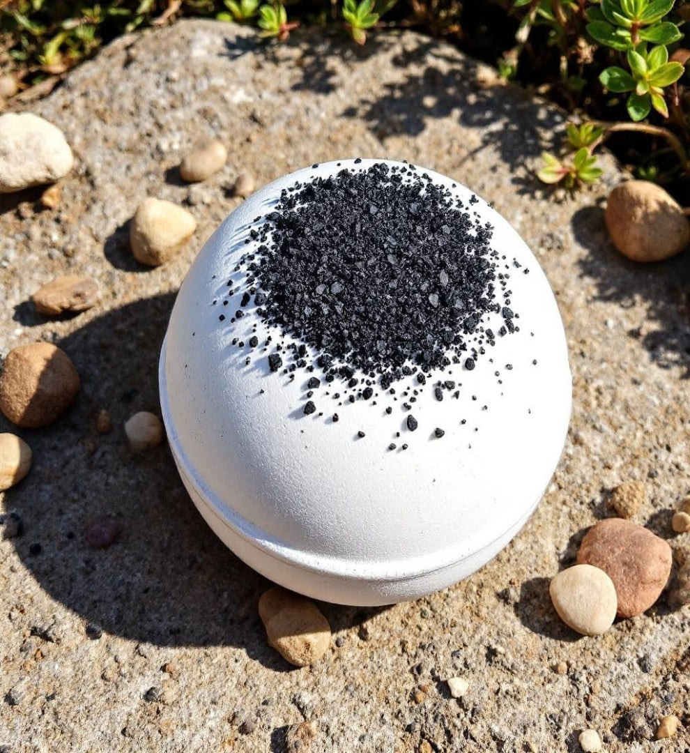 White spherical container with black granules on a sandy surface with small rocks and plants.